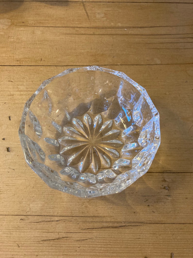 May include: A clear glass bowl with a cut-glass design. The bowl has a starburst pattern in the center and a scalloped edge.