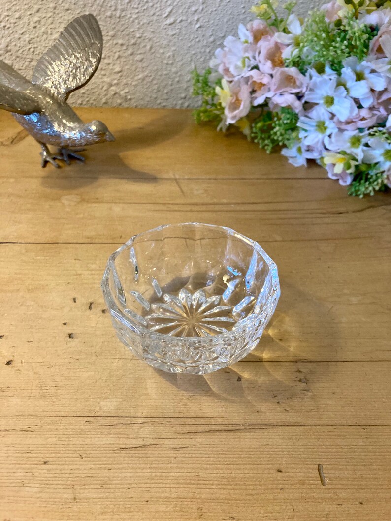 May include: A clear glass bowl with a cut crystal design. The bowl is round and has a wide rim.