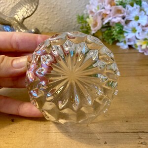 May include: A clear glass bottle stopper with a diamond-shaped pattern. The stopper is round and has a flat bottom.