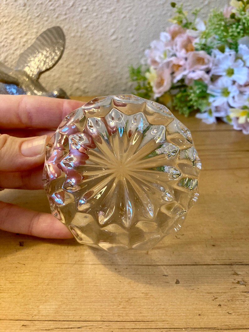 May include: A clear glass bottle stopper with a diamond-shaped pattern. The stopper is round and has a flat bottom.
