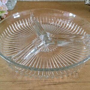 Könnte beinhalten: Eine klare Glasservierplatte mit drei geteilten Abschnitten. Die Platte hat einen geriffelten Rand und ein radiales Muster auf der Unterseite.