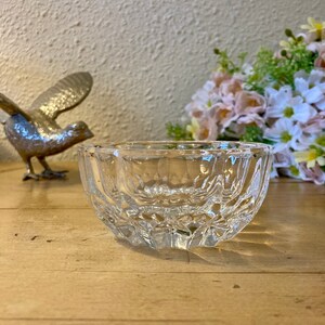 May include: A clear glass bowl with a decorative, faceted design. The bowl is sitting on a wooden surface.