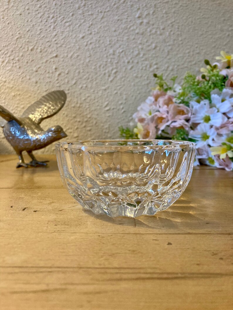 May include: A clear glass bowl with a decorative, faceted design. The bowl is sitting on a wooden surface.