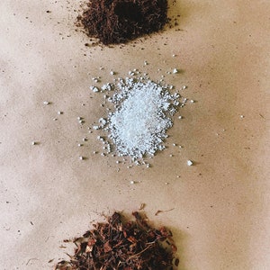 May include: An overhead shot displays three distinct piles of gardening materials. At the top is a dark brown, fibrous substance, followed by a pile of white, granular material, and at the bottom, a pile of brown, shredded pieces.
