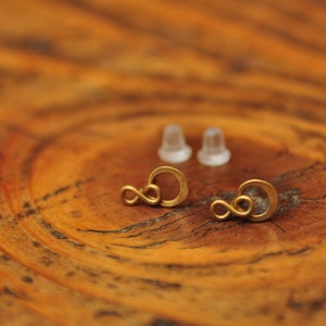 Può includere: Un paio di orecchini a forma di infinito dorati con retro in plastica trasparente.