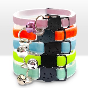 May include: A stack of five colourful cat collars with a bell and a black cat face charm. The collars are in pink, orange, light blue, neon yellow, and light green.