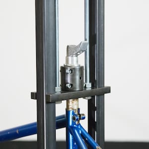 Puede incluir: Un cuadro de bicicleta azul se está presionando en un marco de metal con una palanca y una varilla roscada. El cuadro se está presionando en un marco de metal con una palanca y una varilla roscada.