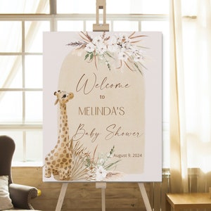 May include: Welcome to Melinda's Baby Shower sign with a giraffe illustration, white flowers, and pampas grass. The date August 9, 2024 is printed on the sign.