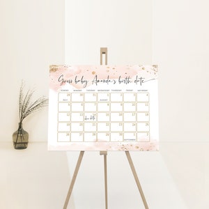 Könnte beinhalten: Ein rosa und goldener Kalender mit dem Text "Guess baby Amanda's birth date" oben. Der Kalender ist für Juli, August und September. Der Geburtstermin ist auf den 14. August markiert.