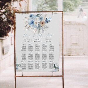 May include: A seating chart for Brian's baptism, displayed on a gold metal stand. The sign features a floral design with blue and beige accents and the text "Please Find Your Seat". The date is 07.09.24.