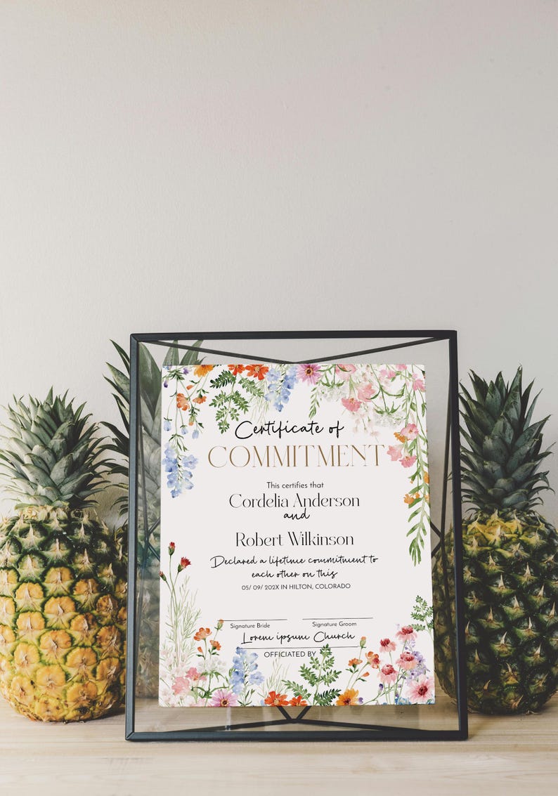 May include: A framed certificate of commitment with floral decorations. The certificate reads "Certificate of Commitment" and lists names and a date. Two pineapples flank the frame.