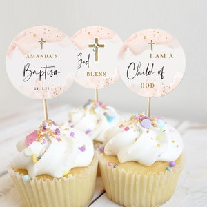Könnte beinhalten: Drei Cupcake-Topper mit einem Aquarellhintergrund in Rosa- und Goldtönen. Die Topper zeigen ein Kreuz mit floralen Akzenten und den Text "Amanda's Baptism 08.11.22", "God Bless" und "I am a Child of God".