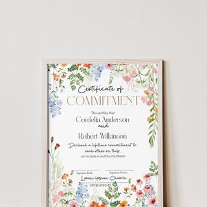 May include: A framed certificate with floral decorations. The text reads "Certificate of Commitment" and lists names and a commitment date. The certificate is in a light wood frame.