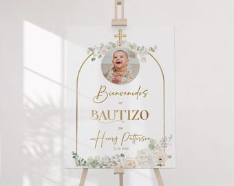 May include: A white rectangular baptism welcome sign on a wooden easel featuring a circular photo of a baby, a gold cross, and green eucalyptus foliage. The text reads Bienvenidos al BAUTIZO de Henry Patterson 12. 10. 202x in gold lettering.