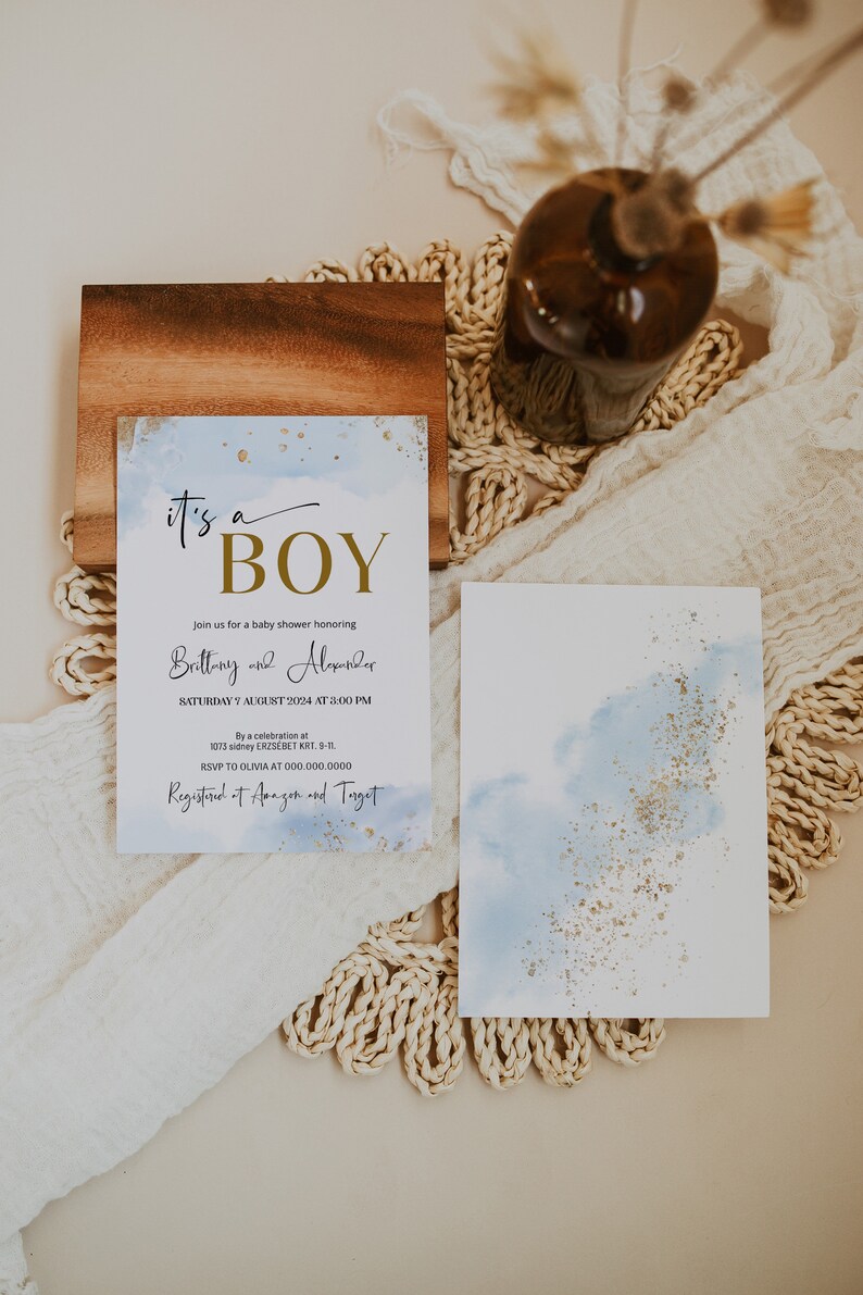 May include: A baby shower invitation with a blue watercolour background and gold glitter. The invitation reads "It's a Boy" in gold lettering and includes the names "Brittany and Alexander", the date "Saturday, 7 August 2024 at 3:00 PM", the address "1073 Sidney Erzs&eacute;bet Krt. 9-11", and the RSVP information "RSVP to Olivia at 000.000.0000". The invitation also states "Registered at Amazon and Target".
