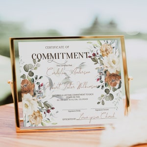 Puede incluir: Un certificado de compromiso enmarcado con detalles florales. El certificado dice "Certificate of Commitment" e incluye nombres, una fecha y un lugar. El marco es de color dorado.