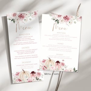 May include: Two rectangular paper menu cards featuring a floral design with dusty pink roses and white pumpkins at the top and bottom. The text reads Menu, Appetizer, Entree, and Dessert, followed by food items like Harvest Green Salad.