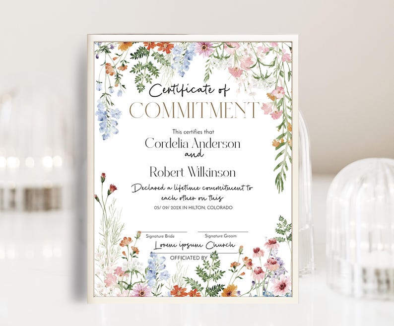 May include: A framed certificate with floral watercolour accents. The text reads "Certificate of COMMITMENT" above the names Cordelia Anderson and Robert Wilkinson. The certificate declares a lifetime commitment.