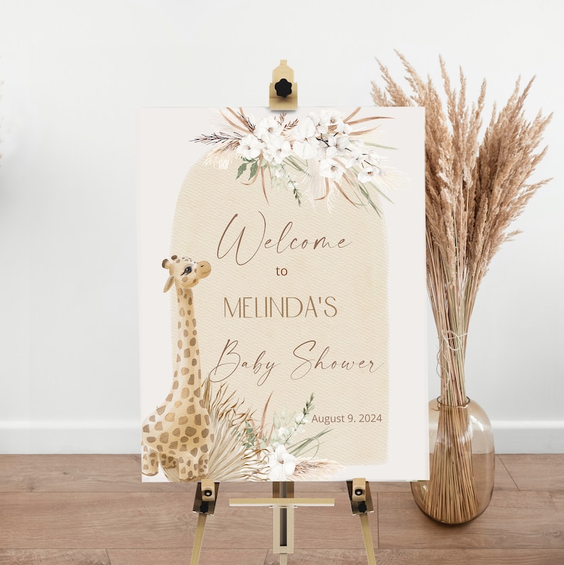 May include: Welcome to Melinda's Baby Shower sign with a cute giraffe illustration, white flowers, and pampas grass. The sign is on a wooden easel and has the date August 9, 2024.
