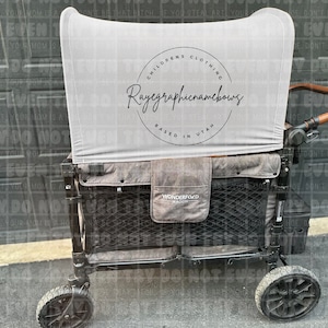 May include: A black wagon with a grey canvas canopy. The canopy has a white circle with the text "Children's Clothing Rayegraphicnamebows Based in Utah". The wagon has a black mesh storage area and a brown handle.