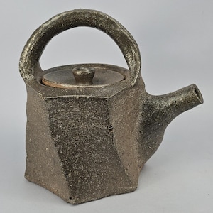 May include: A handcrafted, dark brown ceramic teapot with a geometric design. The teapot features a curved handle, a small lid with a knob, and a spout. The textured surface gives it a rustic, artisanal feel, perfect for brewing tea.