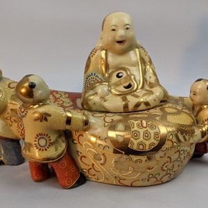 May include: A ceramic incense burner with a gold and white design. A smiling Buddha figure sits on top of the burner, surrounded by four smaller figures.