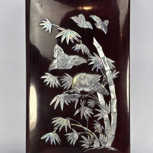 May include: A dark red wooden box with a mother-of-pearl inlay design of birds and bamboo. The birds are in flight and the bamboo is growing tall.