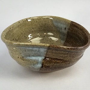 May include: A brown and beige ceramic bowl with a light blue glaze. The bowl has an irregular shape and a slightly uneven rim.