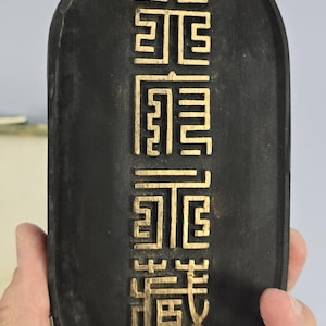 May include: A black inkstone with gold Chinese characters inscribed on the surface. The characters read "龍門", which translates to "Dragon Gate".