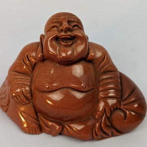 May include: A brown sandstone sculpture of a laughing Buddha sitting with his legs crossed and holding a bag in his lap.