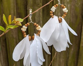 May include: A pair of white flower-shaped earrings with brown wooden beads and white shell beads. The earrings are attached to silver clip-on earring backs.