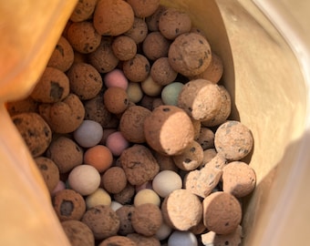 May include: A close-up view of a bag filled with brown, beige, and light blue clay pebbles. The pebbles are used for growing plants in a hydroponic system.