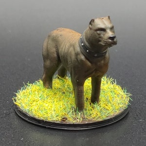 May include: A brown painted miniature dog figurine with a black leather collar, standing on a green and yellow grass base.