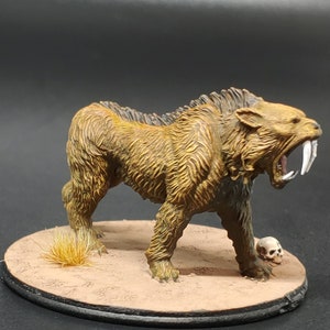 May include: A painted miniature of a saber-toothed cat with a brown and yellow fur, standing on a brown base with a skull.