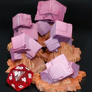 May include: Five pink, cube-shaped, miniature buildings on brown, rocky bases. A red twenty-sided die with white numbers is in the foreground.