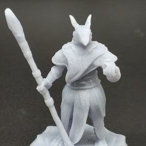 May include: A light gray 3D printed miniature of a humanoid figure with a reptilian head and a long staff. The figure is wearing a long robe and is standing on a round base.