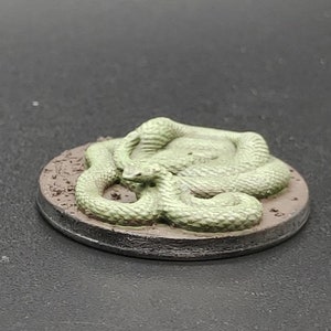 May include: A green snake figurine curled up on a brown base. The snake is painted in a light green color and has a textured surface.
