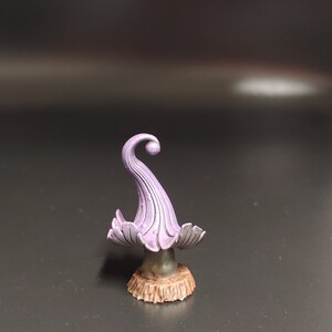 May include: A small, purple, mushroom-shaped figurine with a curled top and a brown base.