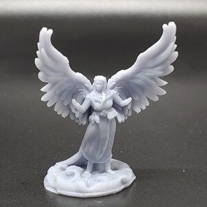 May include: A miniature figurine of a winged female figure with outstretched arms, standing on a cloud-shaped base. The figure is painted in a light gray color.