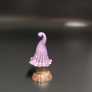 May include: A small purple mushroom figurine with a curled top and a brown base. The mushroom is made of a smooth, painted material.