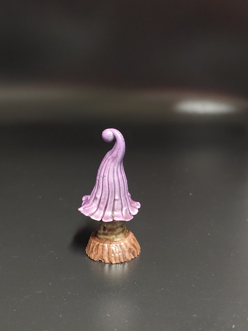 May include: A small purple mushroom figurine with a curled top and a brown base. The mushroom is made of a smooth, painted material.