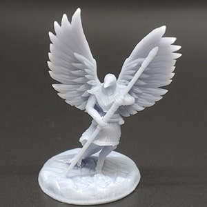 May include: A light gray figurine of an angel with large, detailed wings, holding a staff. The angel stands on a circular base with a textured surface. The figure is a detailed representation of a mythological or fantasy character.