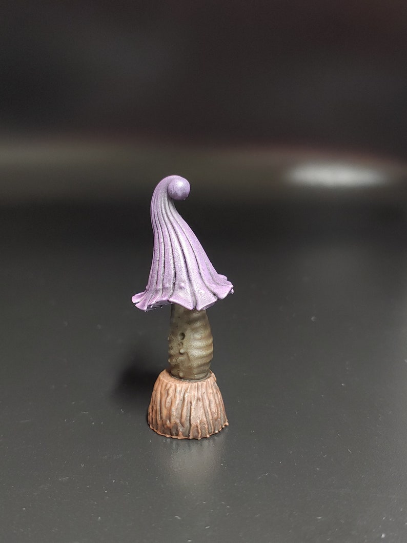 May include: A small purple and brown mushroom figurine with a curled top. The mushroom is painted with a light brown base and a darker brown stem. The top of the mushroom is a vibrant purple color.