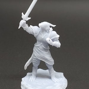 May include: A white 3D printed miniature figurine of a humanoid figure with reptilian features, wearing armor and holding a sword. The figure is standing on a round base.
