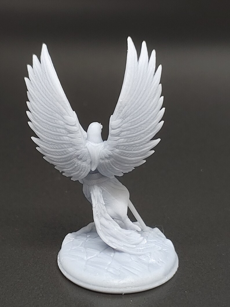 May include: A light grey figurine of a bird with large, detailed wings, perched on a textured base. The bird is sculpted in a stylized pose, with its wings spread wide. The figurine is made of a smooth material.