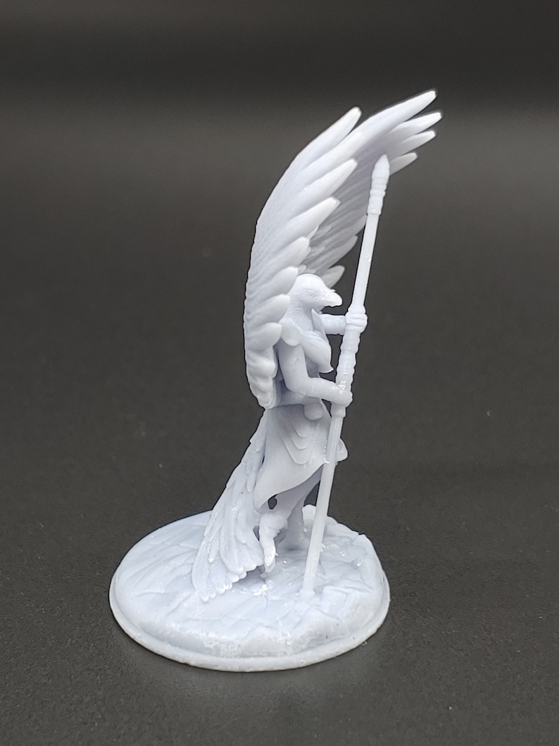 May include: A pale blue figurine of a winged humanoid figure holding a staff. The figure has large, detailed wings and is standing on a circular base. The figurine is likely a fantasy or mythological character.