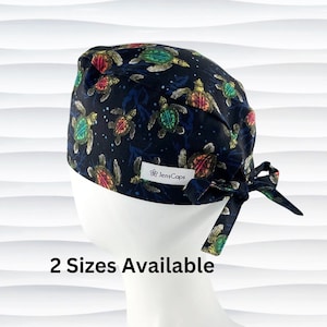 May include: A black scrub cap with a colorful sea turtle print. The cap has a tie at the back and the text "JensCaps" is printed on the front.