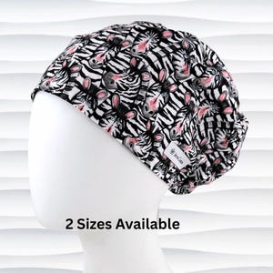 May include: A black and white patterned cap featuring a zebra face design with pink and blue accents. The cap is on a white mannequin head. The text "2 Sizes Available" is below the cap.