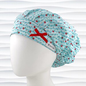 May include: A light blue scrub cap with a floral and striped pattern, accented with a red bow. The cap features small red roses and the text "JensCaps" on a white label.