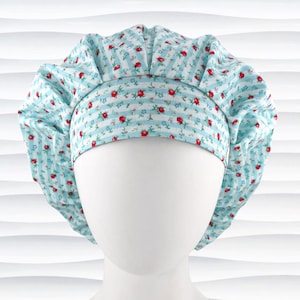 May include: A light blue and white striped bouffant surgical scrub cap with a floral pattern of red roses. The cap is designed to cover the hair and is made of a soft, patterned fabric. The cap is shown on a white mannequin head.